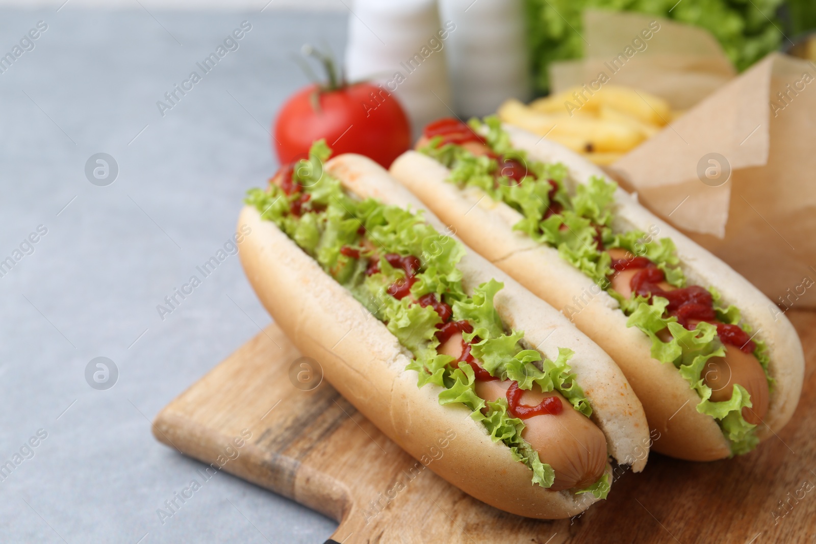 Photo of Tasty hot dogs with lettuce, ketchup and potato fries on light grey table, closeup