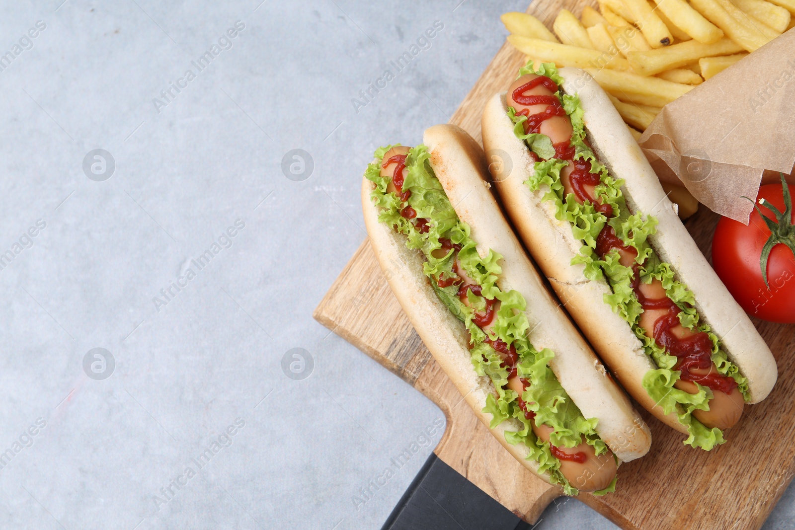 Photo of Tasty hot dogs with lettuce, ketchup and potato fries on light grey table, top view. Space for text