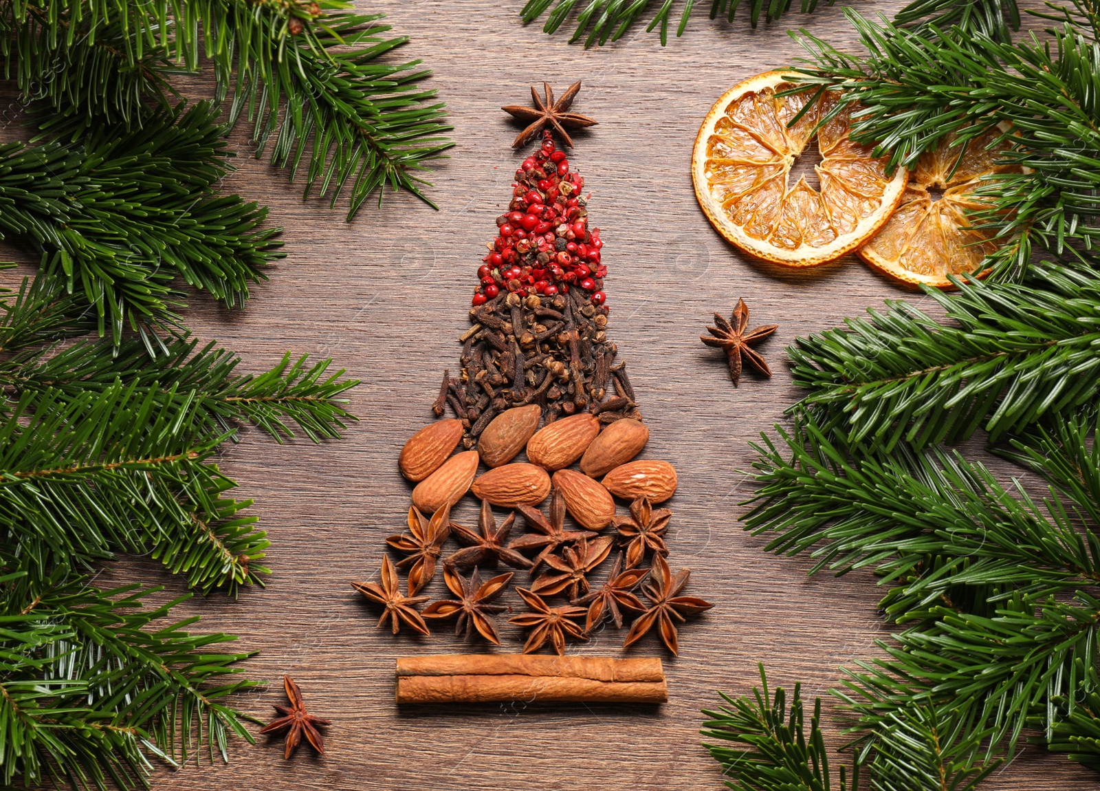 Photo of Christmas tree made of different spices, dried orange slices and fir branches on wooden table, flat lay