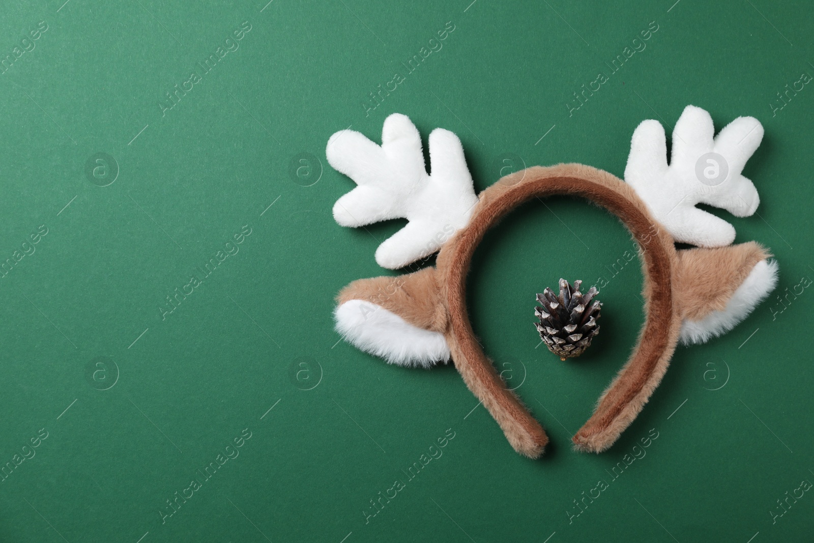 Photo of Beautiful reindeer headband and conifer cone on green background, top view with space for text. Christmas accessory