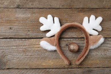 Photo of Beautiful reindeer headband and Christmas bauble on wooden background, top view. Space for text