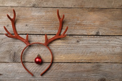 Photo of Beautiful reindeer headband and Christmas bauble on wooden background, top view. Space for text