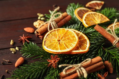 Photo of Different spices, dried orange slices and fir tree branches on wooden table, closeup. Christmas season