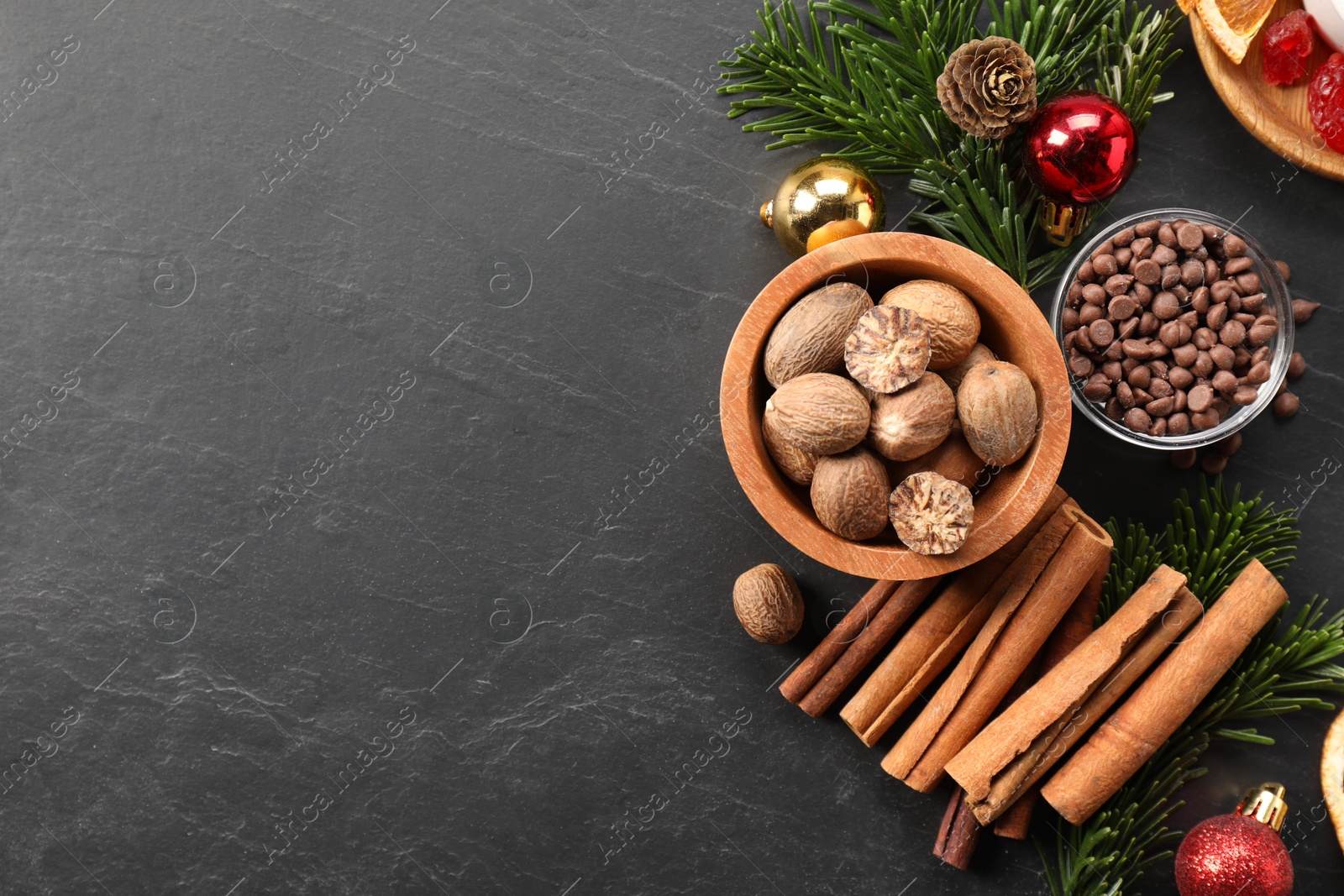 Photo of Different aromatic spices and fir tree branches on black table, flat lay with space for text. Christmas season