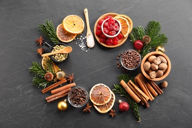 Photo of Frame of different aromatic spices and fir tree branches on black table, flat lay. Christmas season