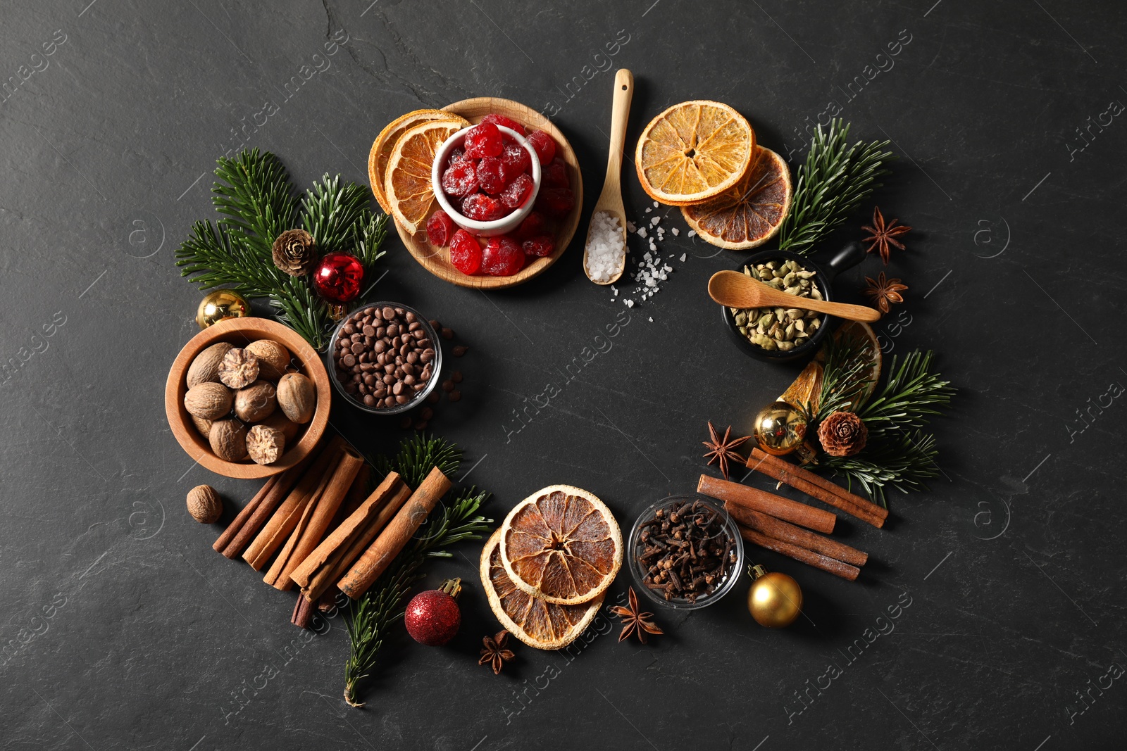 Photo of Frame of different aromatic spices and fir tree branches on black table, flat lay. Christmas season