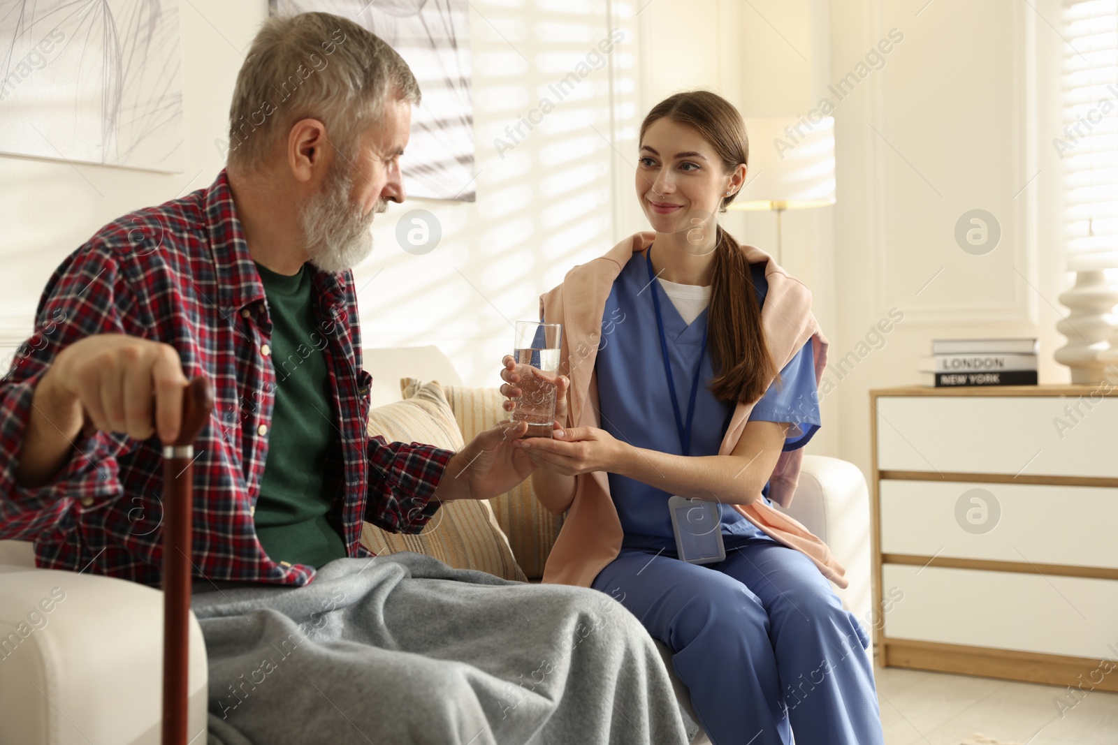 Photo of Caregiver giving glass of water to senior man indoors. Home health care service