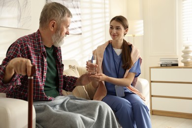 Photo of Caregiver giving glass of water to senior man indoors. Home health care service