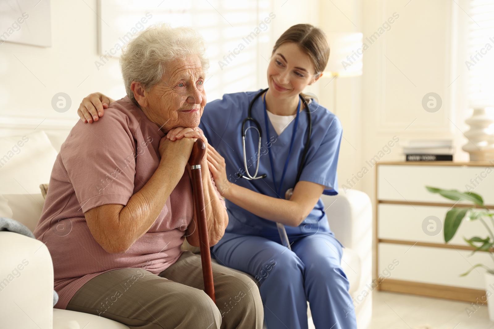 Photo of Caregiver supporting senior woman on sofa. Home health care service