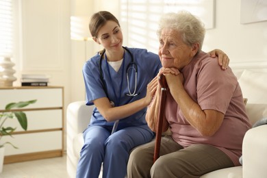 Photo of Caregiver supporting senior woman on sofa. Home health care service