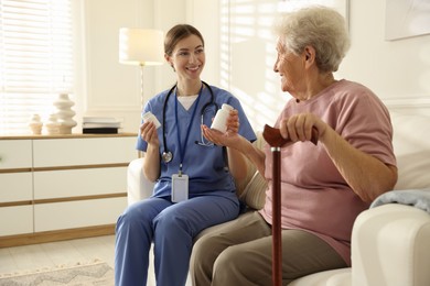 Photo of Caregiver giving pills to senior woman on sofa indoors. Home health care service