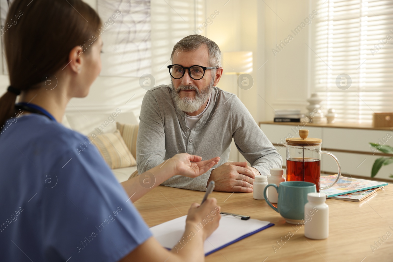 Photo of Caregiver examining senior man at table indoors. Home health care service