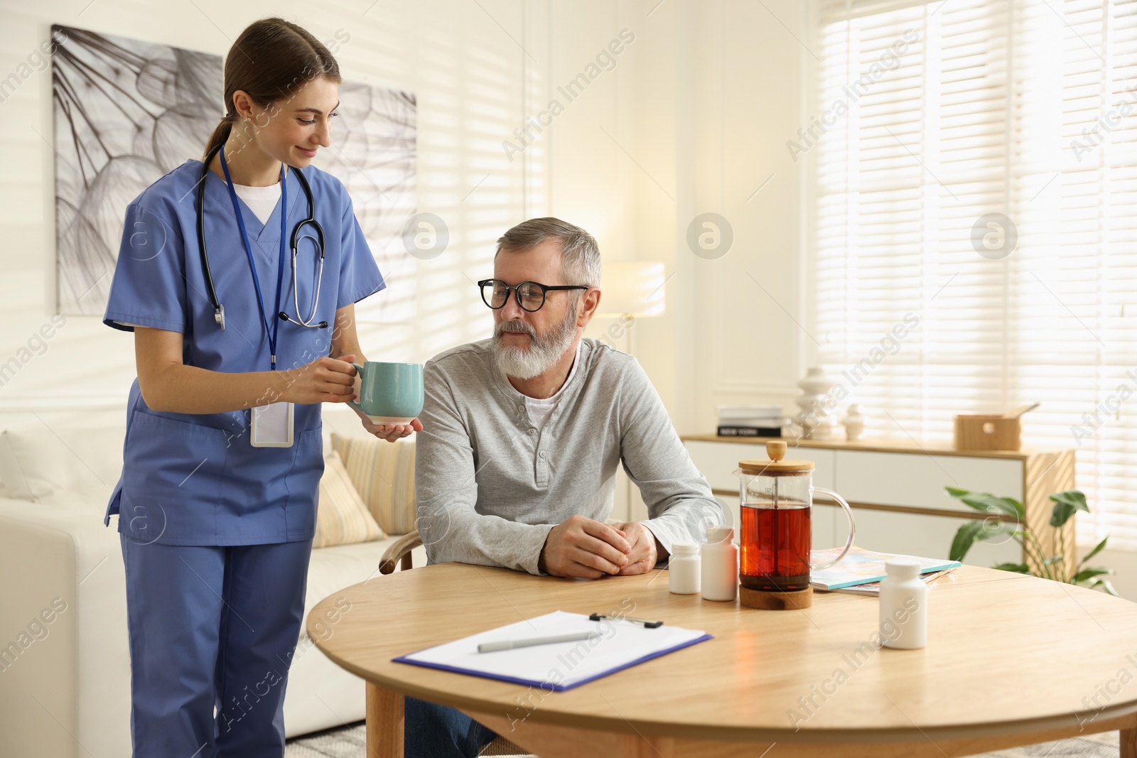 Photo of Caregiver giving cup of drink to senior man indoors. Home health care service