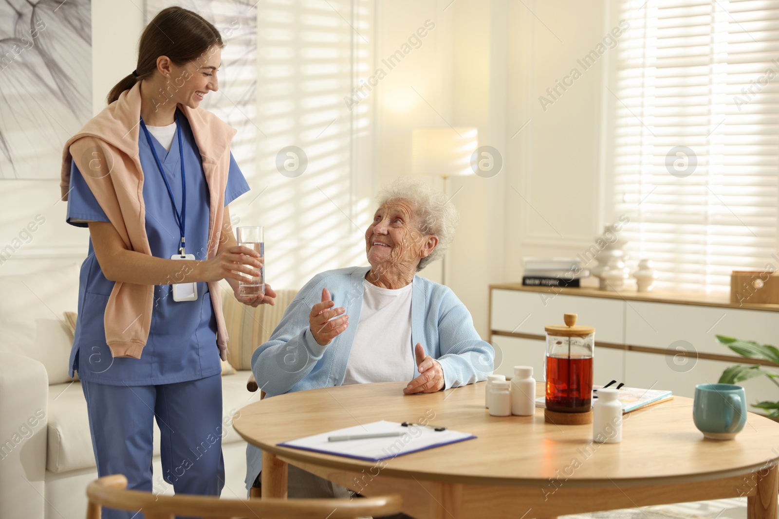 Photo of Caregiver giving glass of water to senior woman indoors. Home health care service