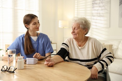 Photo of Caregiver measuring patient's blood pressure at table indoors. Home health care service