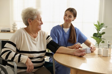 Photo of Caregiver measuring patient's blood pressure at table indoors. Home health care service