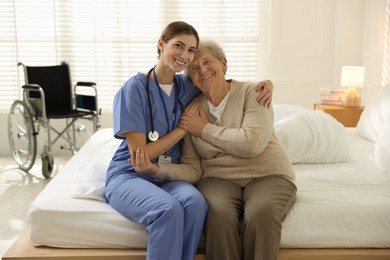 Photo of Caregiver supporting senior woman on bed indoors. Home health care service