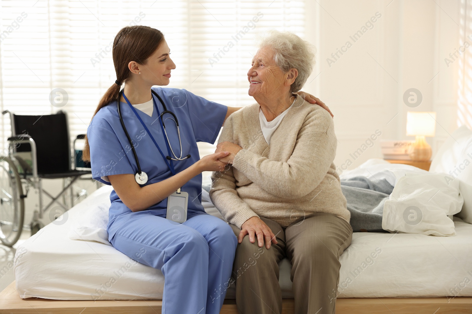 Photo of Caregiver supporting senior woman on bed indoors. Home health care service