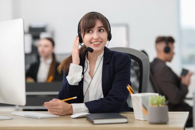 Photo of Saleswoman making notes while talking to client via headset at desk in office