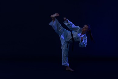 Photo of Young woman in kimono practicing karate on dark background