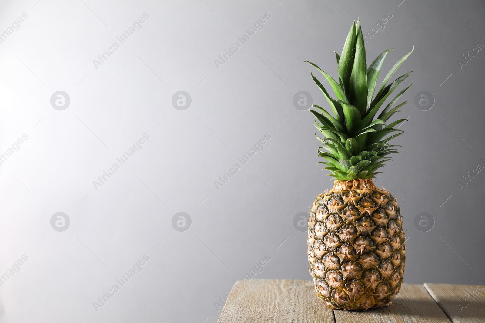 Photo of Fresh ripe pineapple on wooden table against light grey background. Space for text