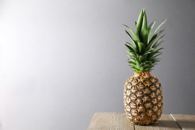 Photo of Fresh ripe pineapple on wooden table against light grey background. Space for text