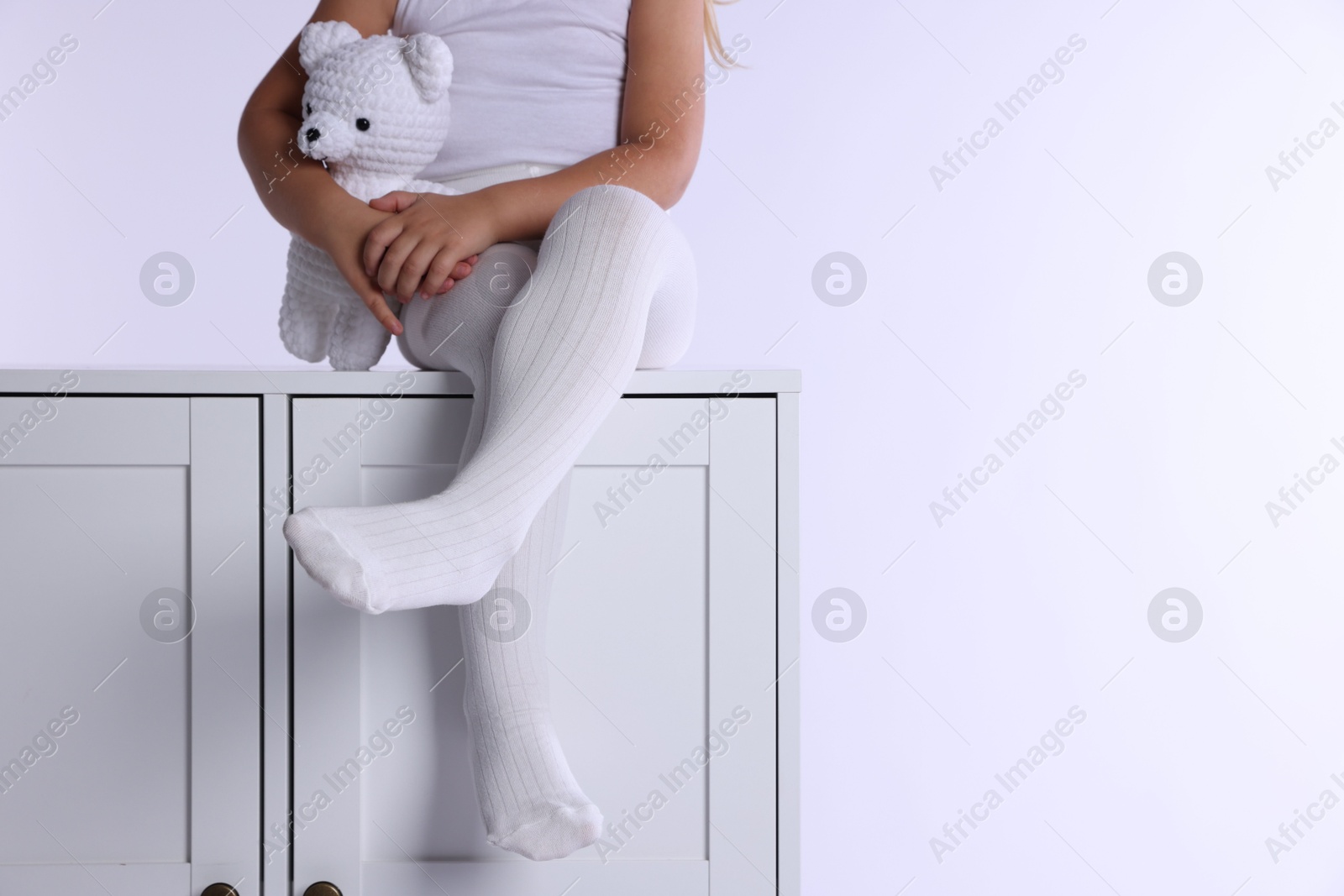 Photo of Child in tights sitting on cabinet against white background, closeup. Space for text