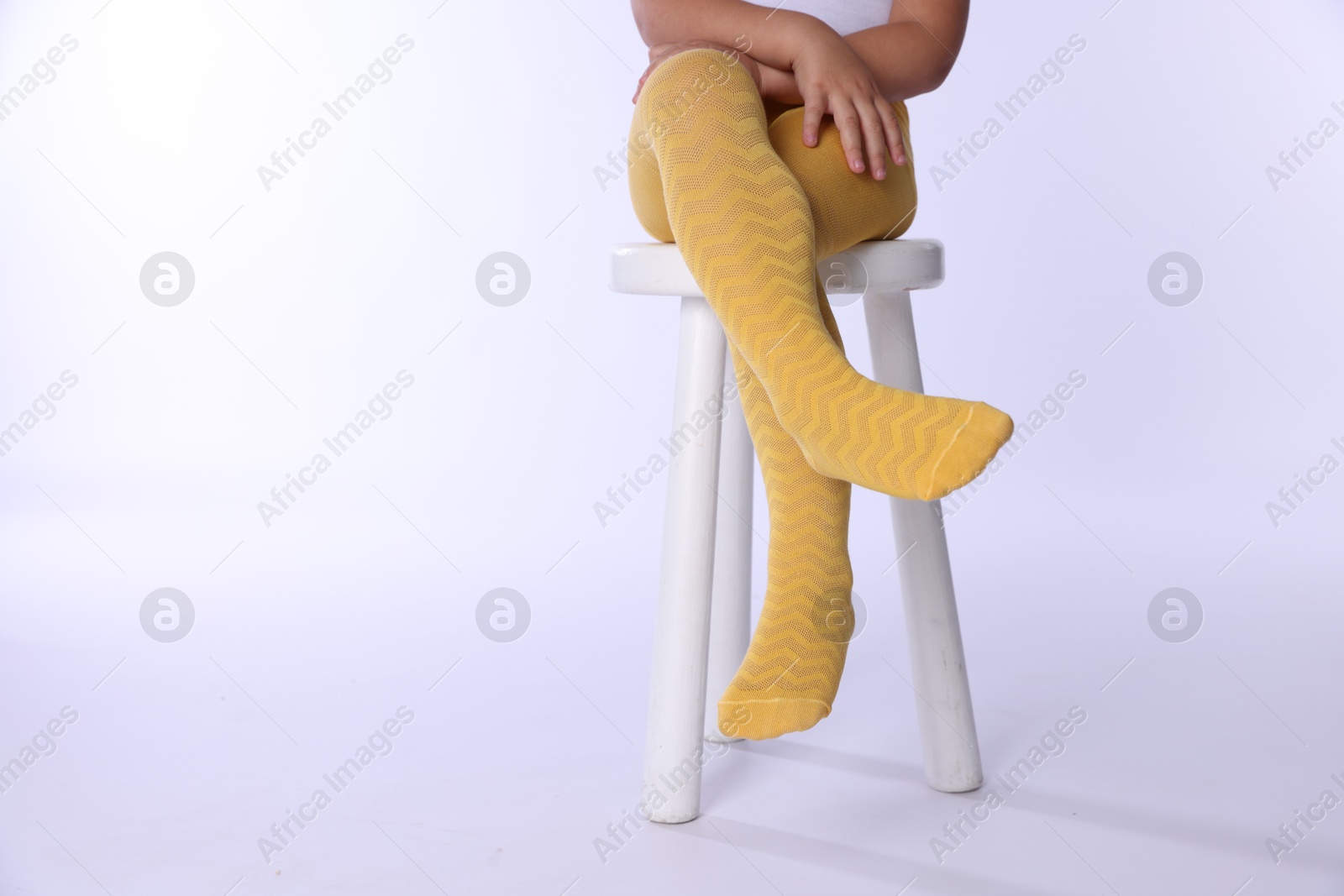 Photo of Child in bright tights sitting on stool against white background, closeup. Space for text