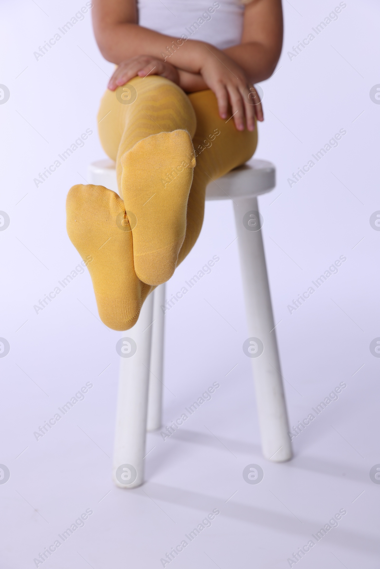 Photo of Child in bright tights sitting on stool against white background, closeup