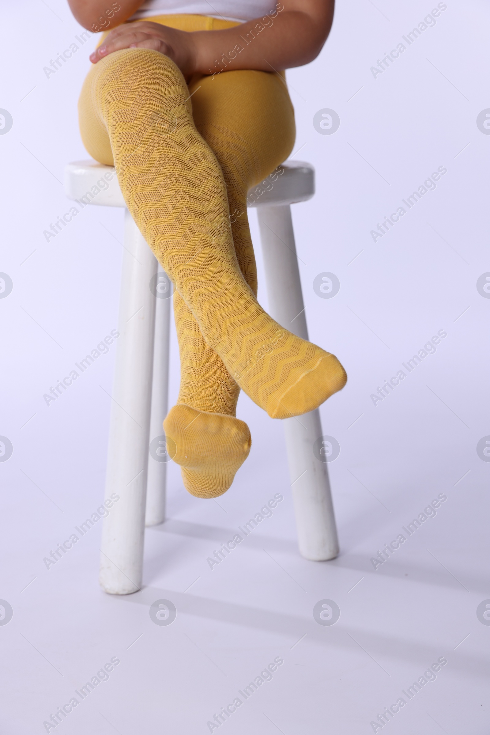 Photo of Child in bright tights sitting on stool against white background, closeup