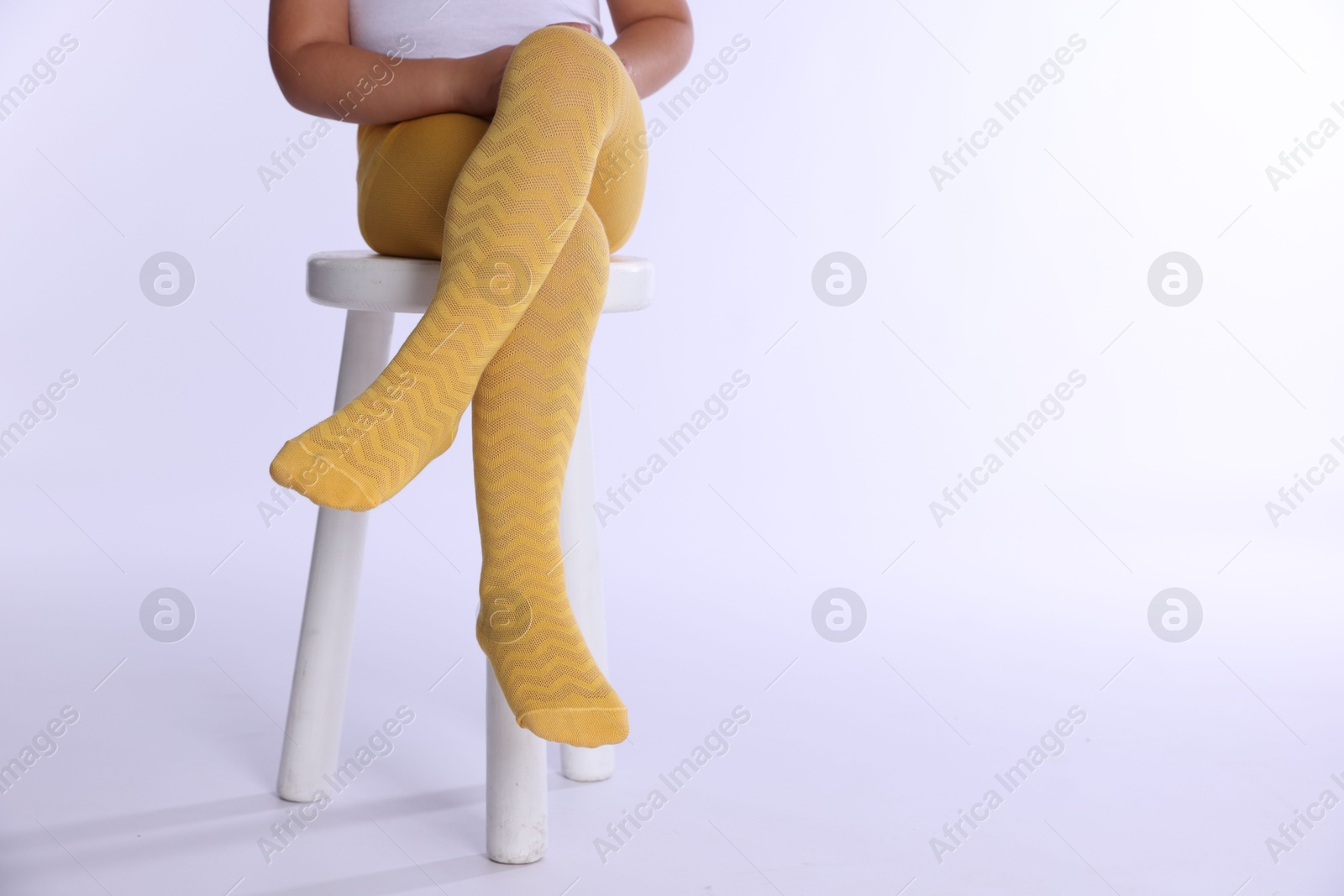 Photo of Child in bright tights sitting on stool against white background, closeup. Space for text