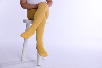 Photo of Child in bright tights sitting on stool against white background, closeup. Space for text