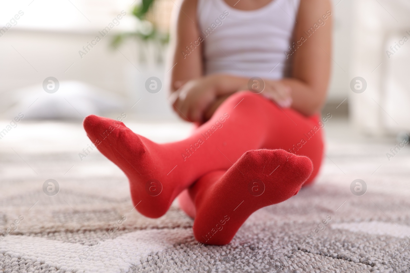 Photo of Child in red tights sitting on floor at home, closeup