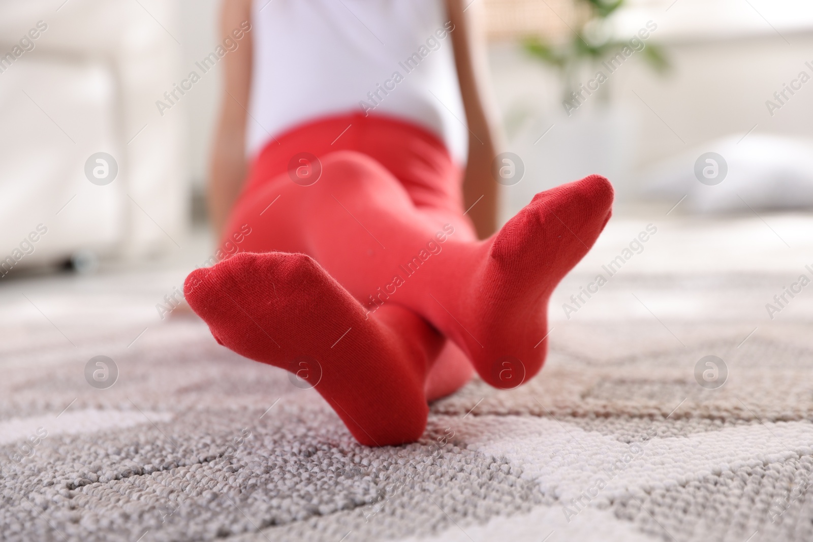 Photo of Child in red tights sitting on floor at home, closeup