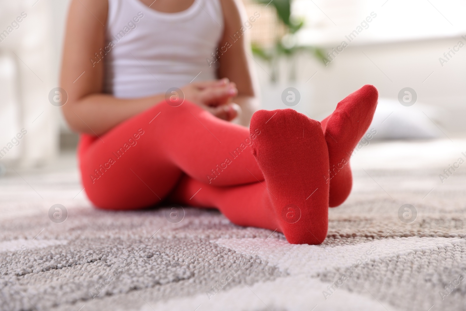 Photo of Child in red tights sitting on floor at home, closeup