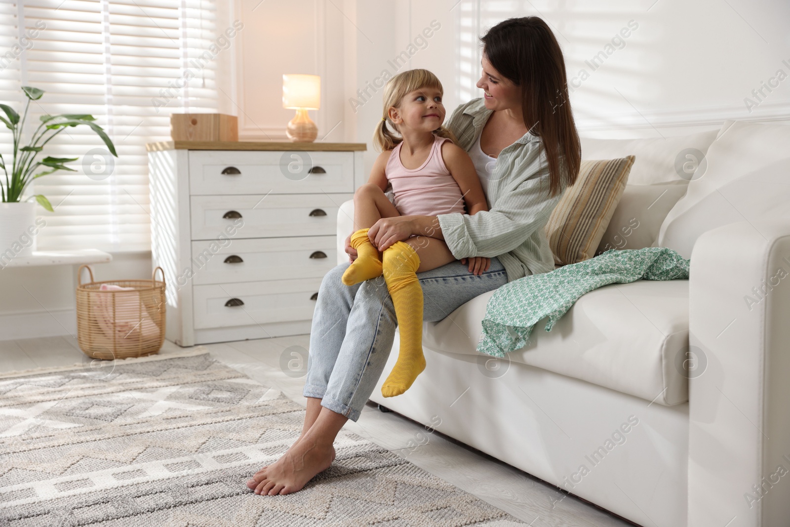 Photo of Mother helping her daughter to put tights on at home. Space for text