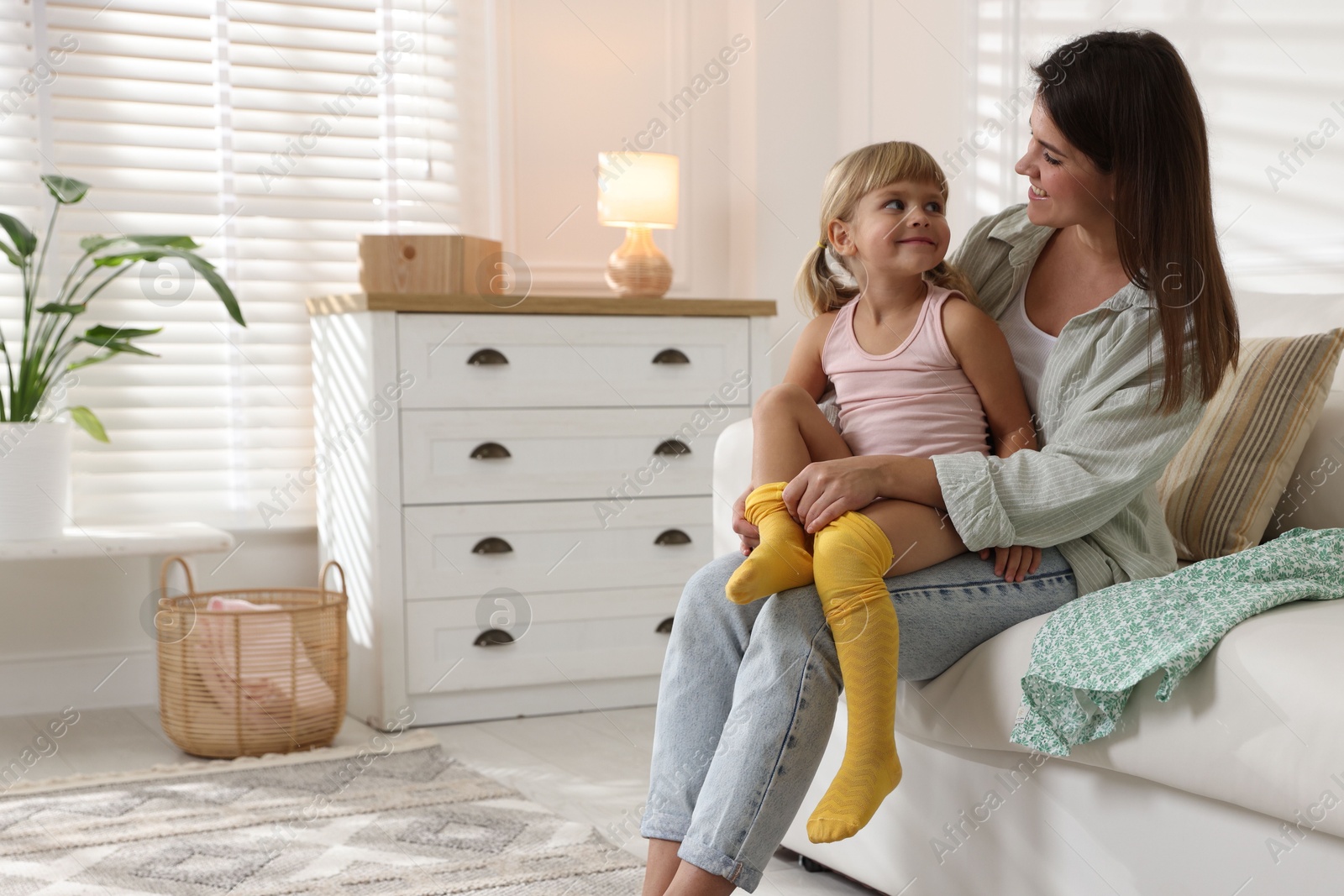 Photo of Mother helping her daughter to put tights on at home. Space for text