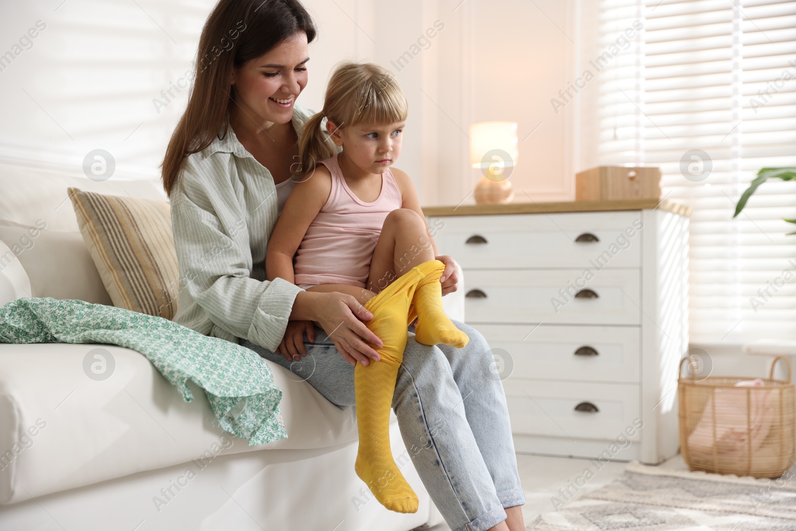 Photo of Mother helping her daughter to put tights on at home. Space for text