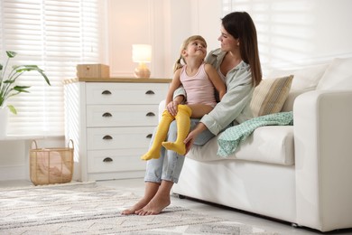 Photo of Mother helping her daughter to put tights on at home. Space for text