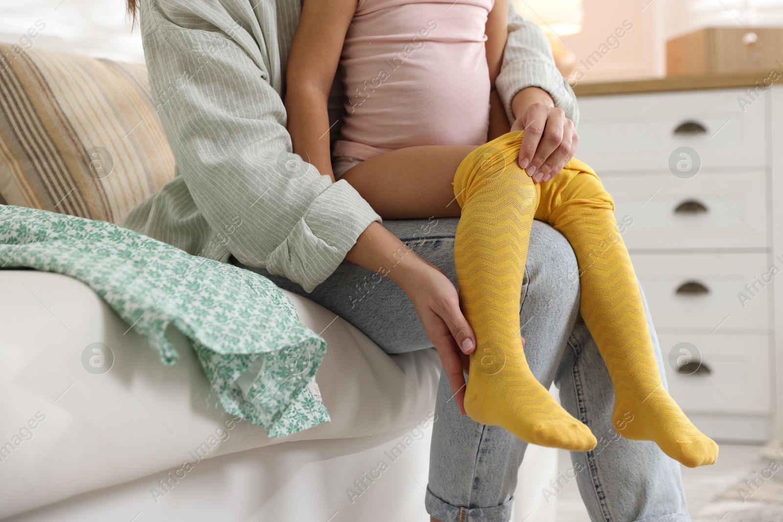 Photo of Mother helping her daughter to put tights on at home, closeup. Space for text