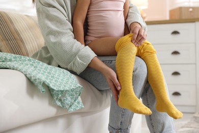 Photo of Mother helping her daughter to put tights on at home, closeup. Space for text