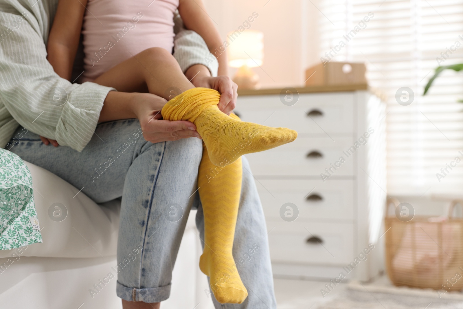 Photo of Mother helping her daughter to put tights on at home, closeup. Space for text