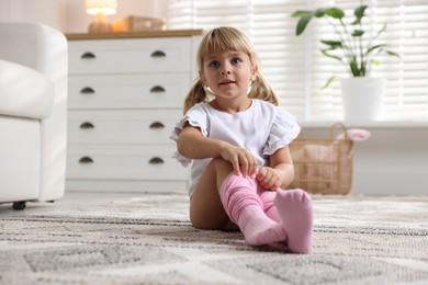 Photo of Little girl putting on soft tights at home