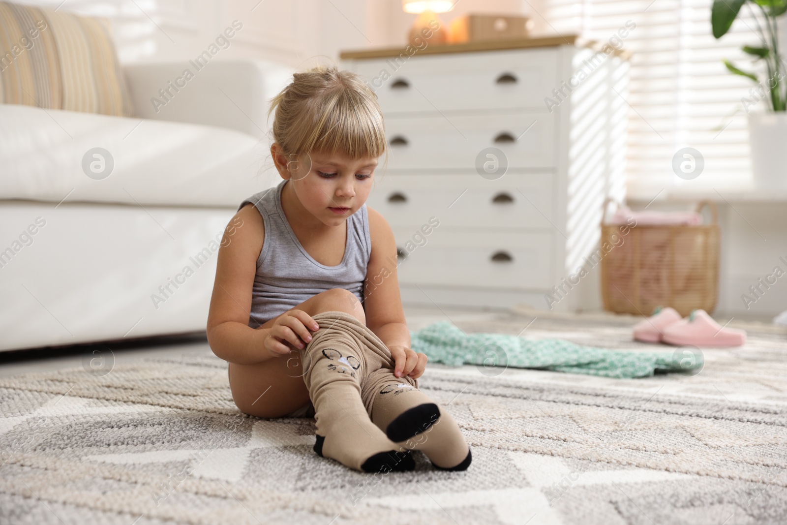 Photo of Little girl putting on soft tights at home. Space for text