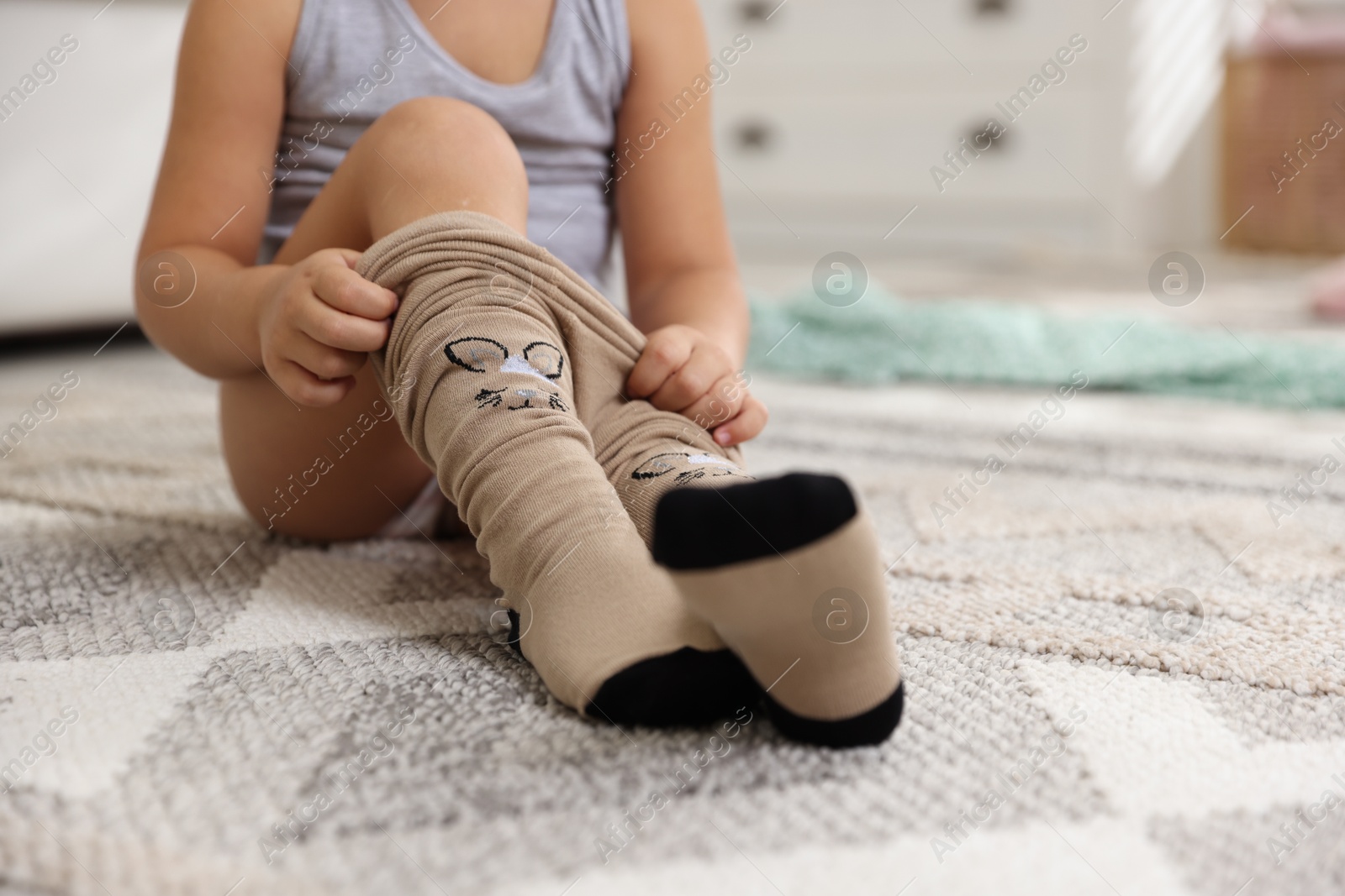 Photo of Little girl putting on soft tights at home, closeup