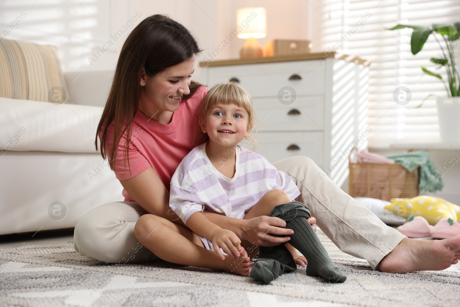 Photo of Mother helping her daughter to put tights on at home