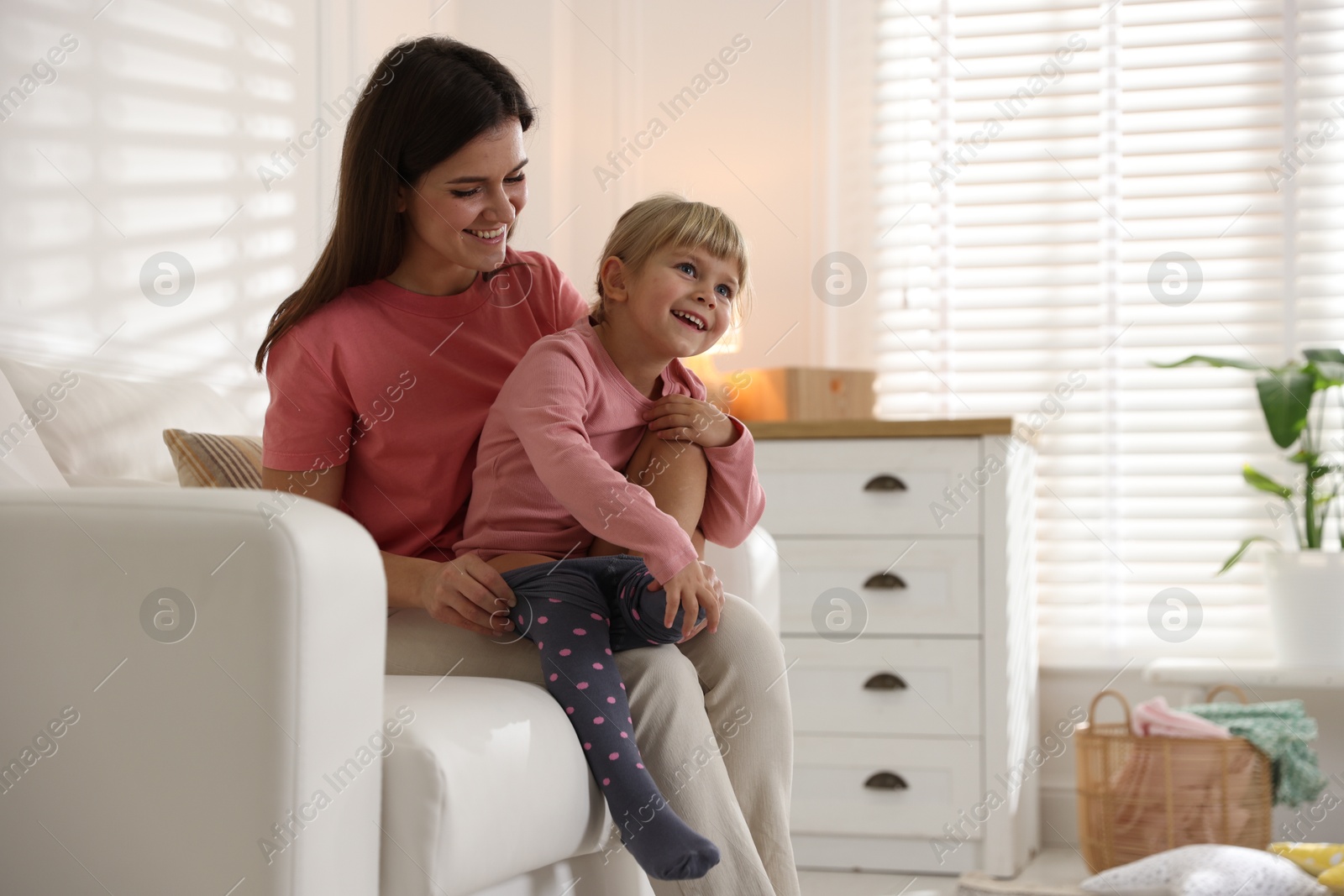 Photo of Mother helping her daughter to put tights on at home. Space for text