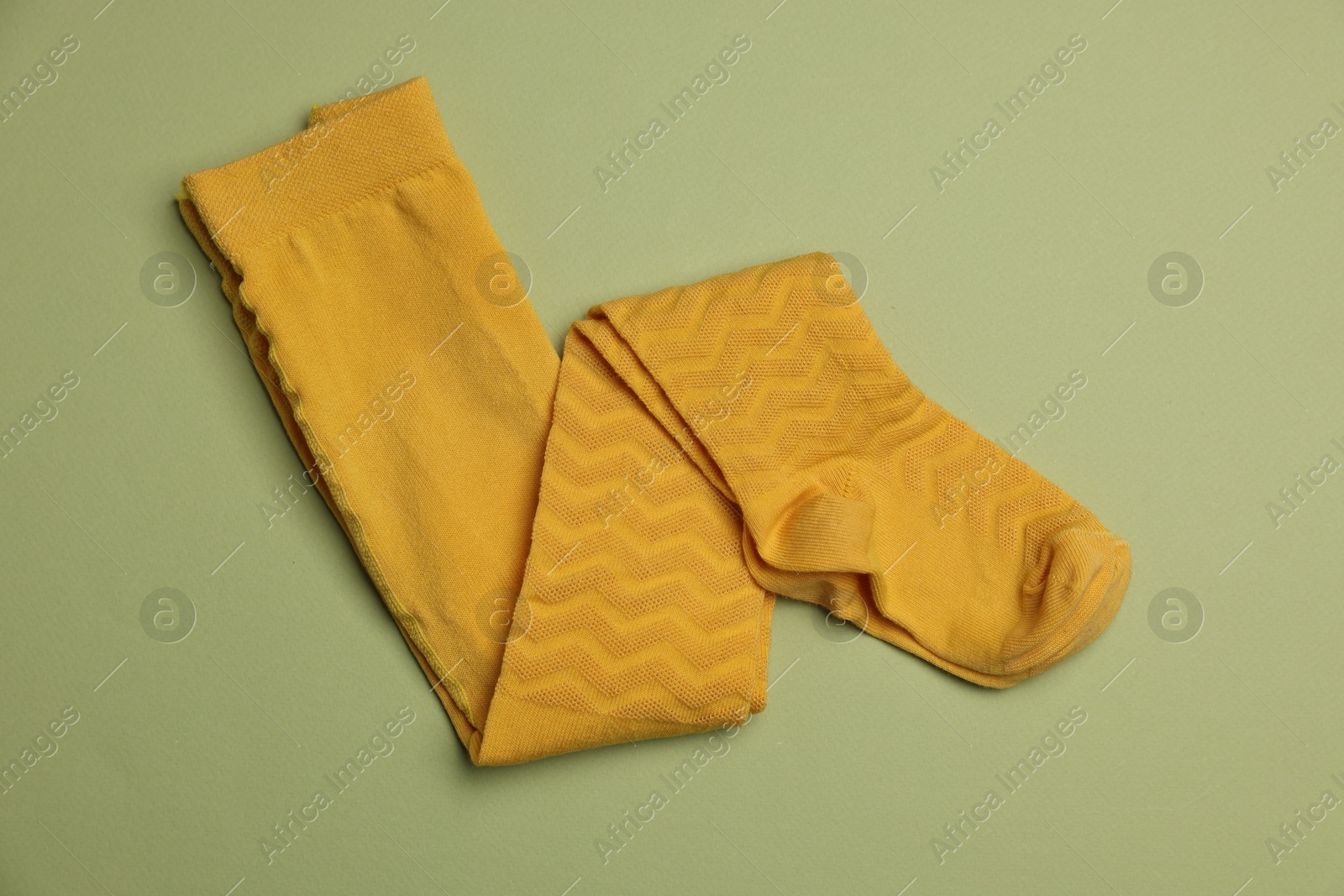 Photo of Beautiful yellow child's tights on green background, top view