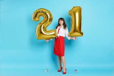 Photo of Coming of age party - 21st birthday. Young woman holding number shaped balloons on light blue background