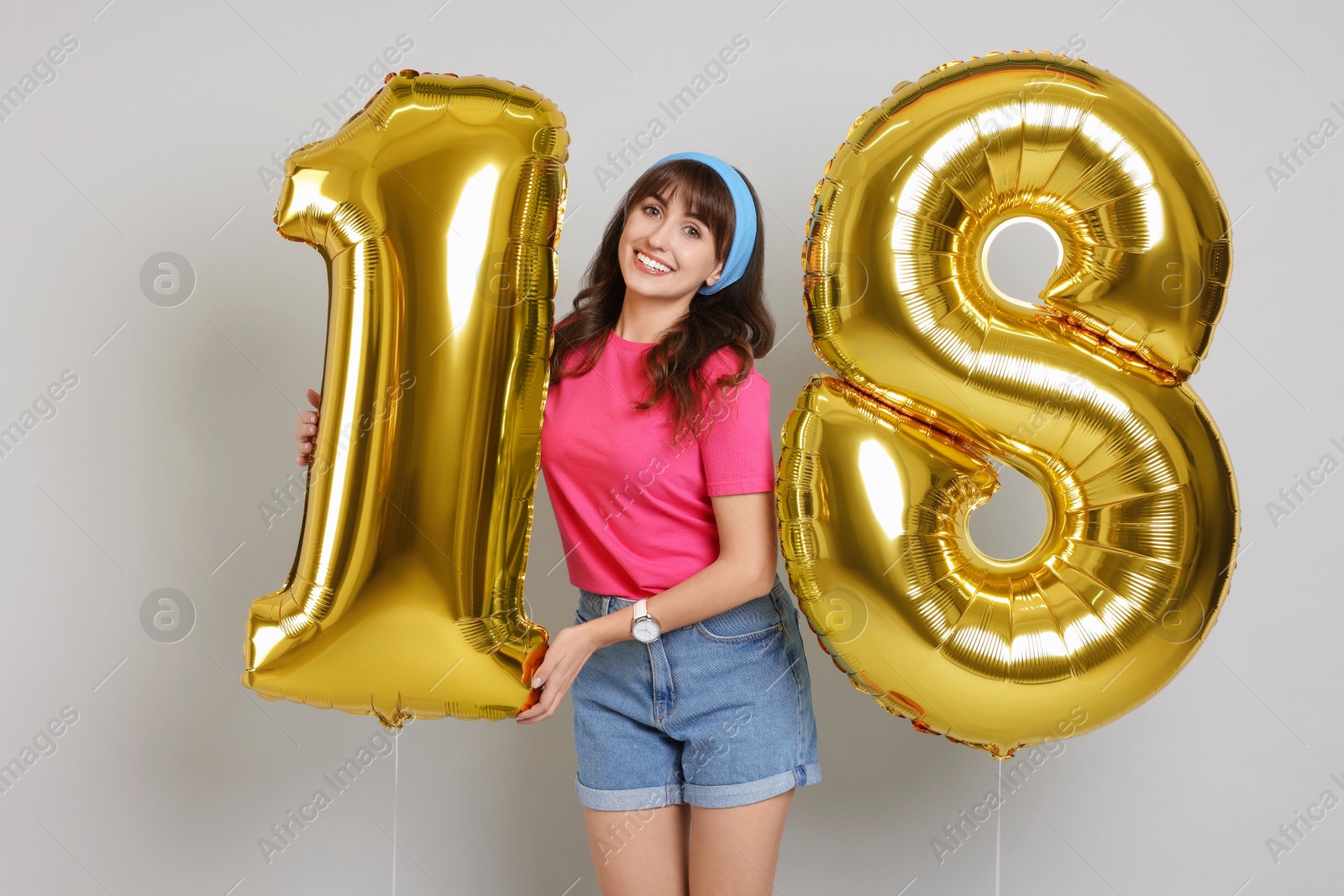 Photo of Coming of age party - 18th birthday. Young woman holding number shaped balloons on light grey background